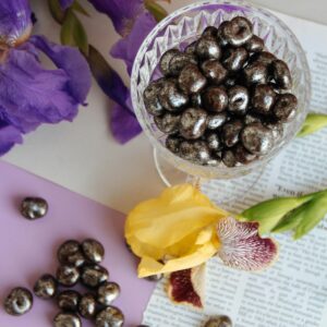 Aesthetic display of chocolate-covered nuts in crystal glass with purple and yellow iris flowers.