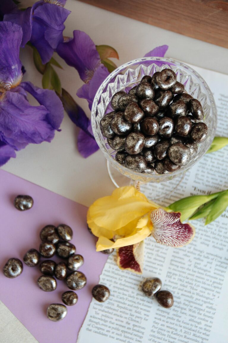 Aesthetic display of chocolate-covered nuts in crystal glass with purple and yellow iris flowers.