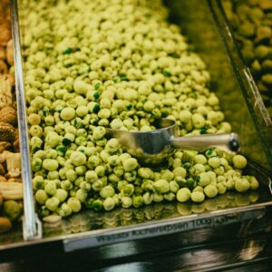 A vertical shot of a bulk bin filled with fresh wasabi peas in a grocery store setting.