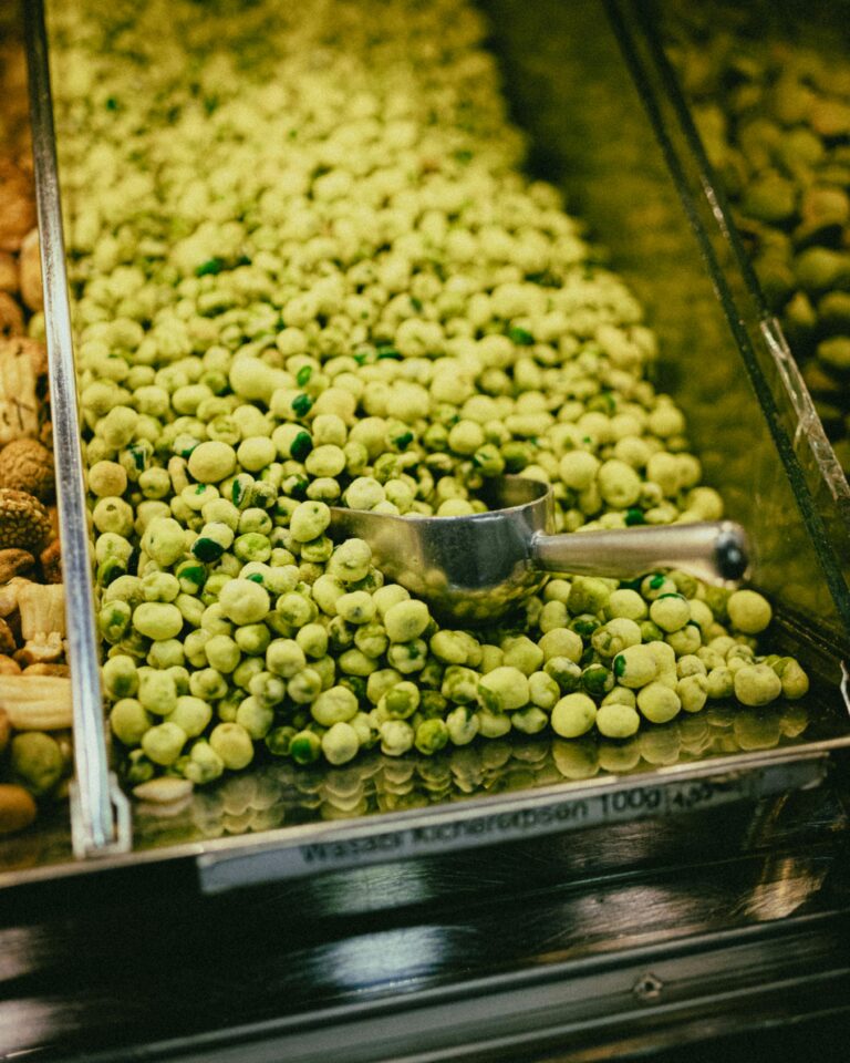 A vertical shot of a bulk bin filled with fresh wasabi peas in a grocery store setting.