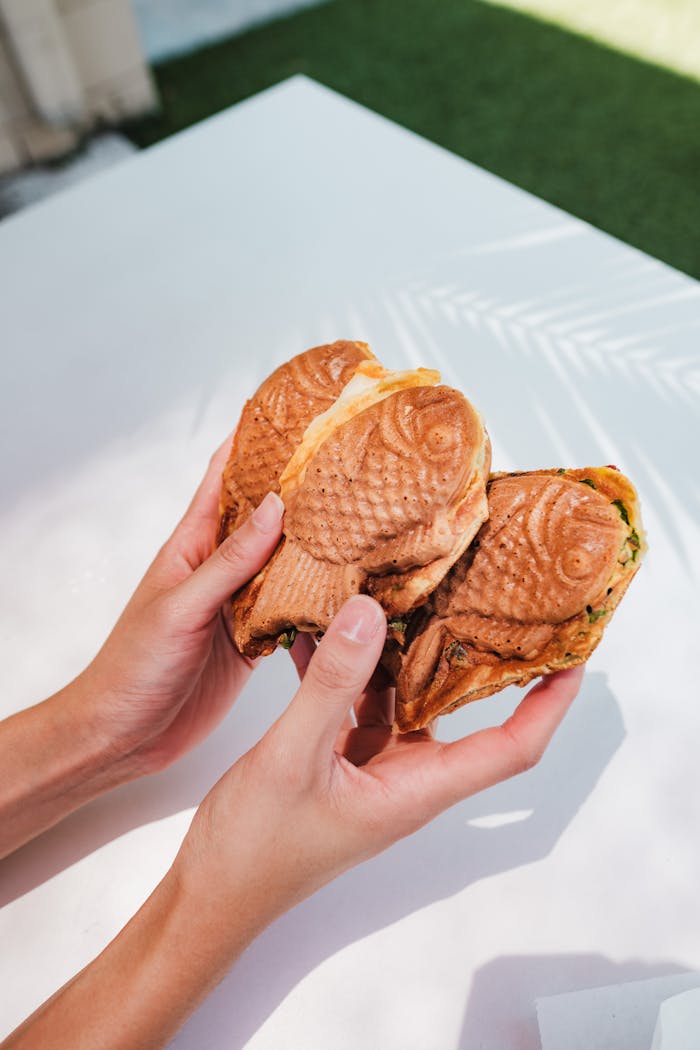 Close-up of hands holding taiyaki waffles outdoors in daylight, showcasing Japanese street food delight.