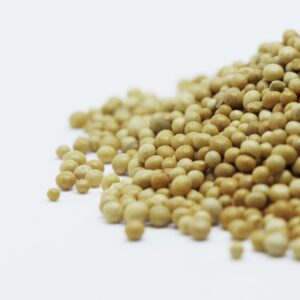 A close-up image showing a pile of brown mustard seeds on a white surface, highlighting their texture and color.
