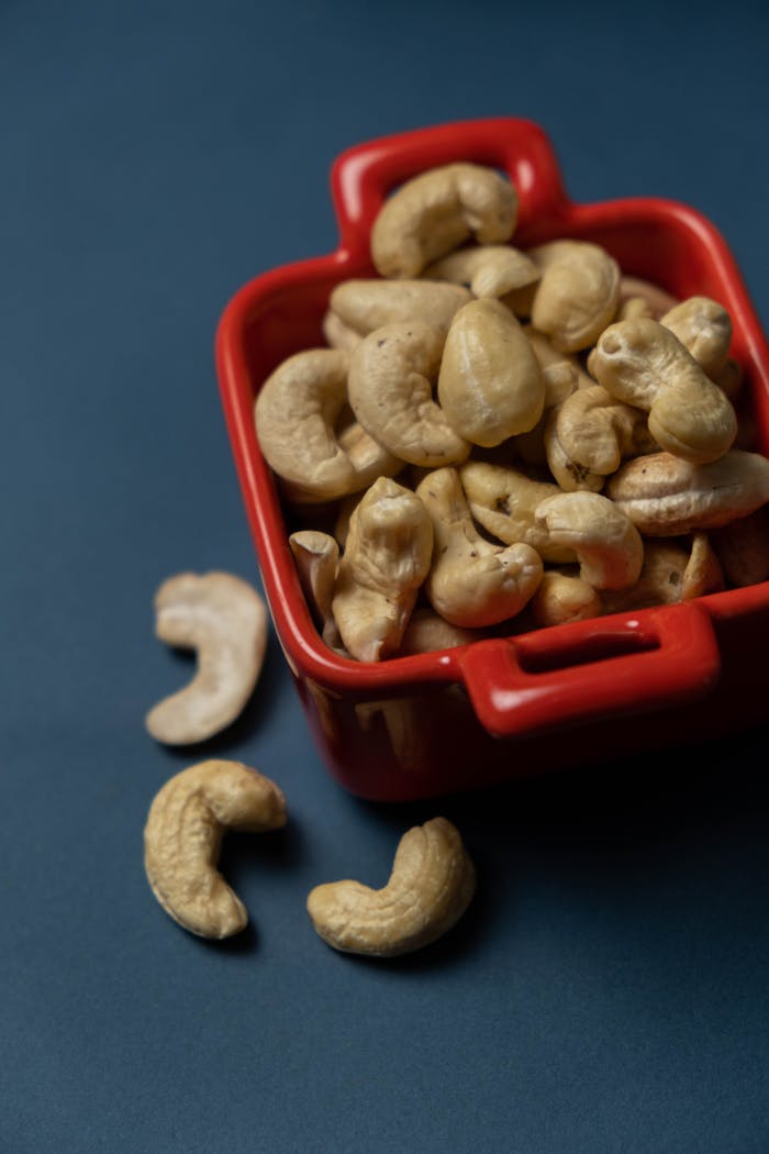 Close-up of organic cashews in a red bowl on a dark background, highlighting healthy snacking.