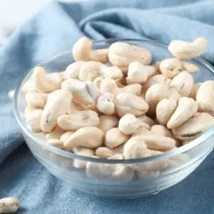 A glass bowl filled with raw cashews on a blue cloth, perfect for healthy snacking.