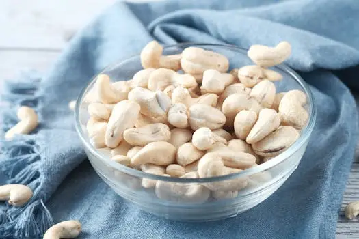 pexels photo 9017852 9017852 A glass bowl filled with raw cashews on a blue cloth, perfect for healthy snacking.